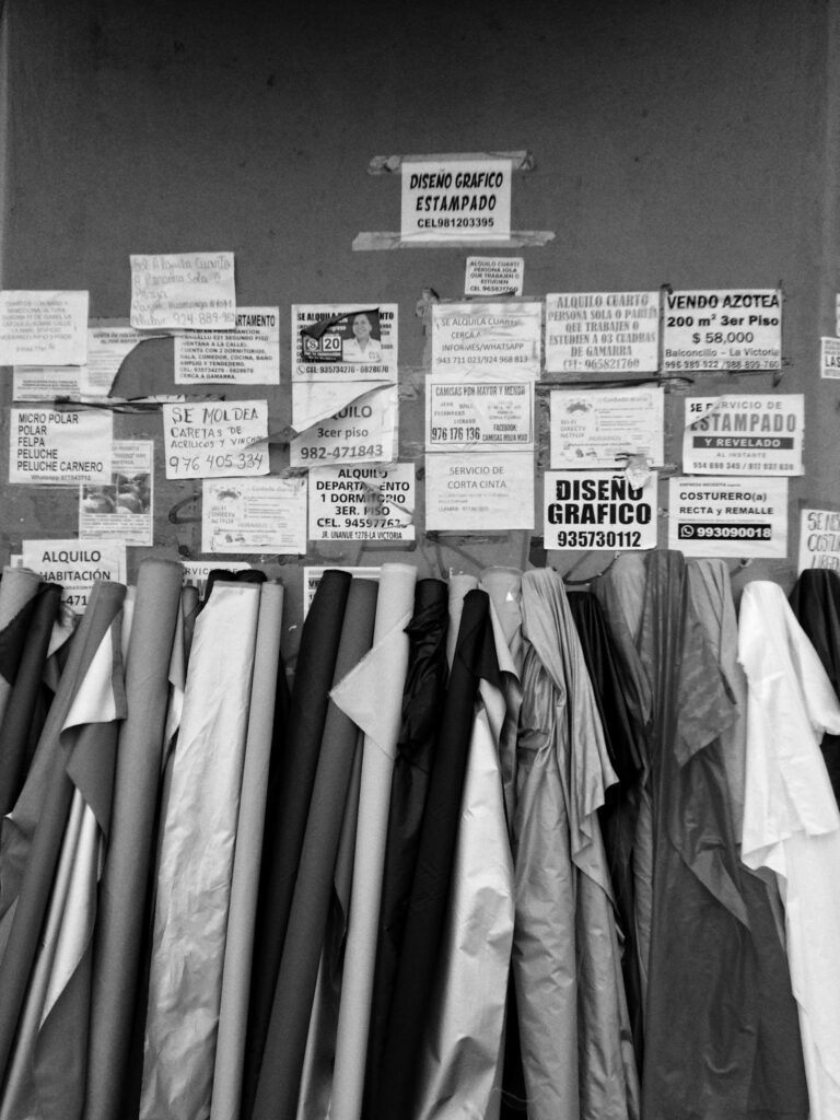 Black and white image of fabric rolls with various posters on a noticeboard in Perú.